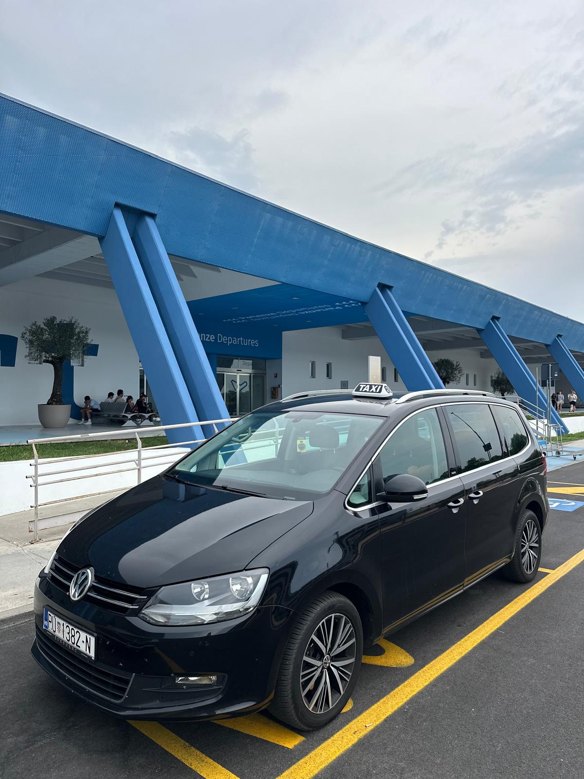 Black VW Sharan taxi with a TAXI roof sign parked outside Pula Airport departures